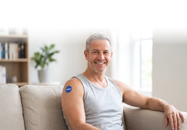 Smiling man in his fifties on a sofa wearing a round blue Averos patch